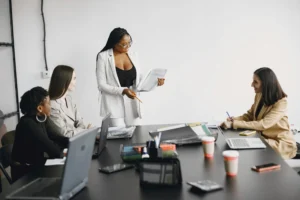 A imagem mostra um grupo de quatro mulheres em uma reunião de negócios em um escritório moderno
