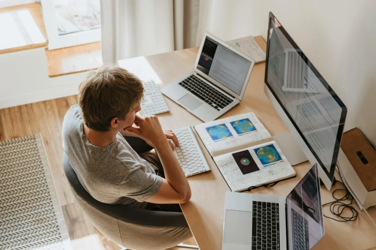 Profissional trabalhando remotamente em estação com múltiplos computadores, representando gestão de ativos de TI da NetEye fora do escritório e monitoramento remoto de dispositivos